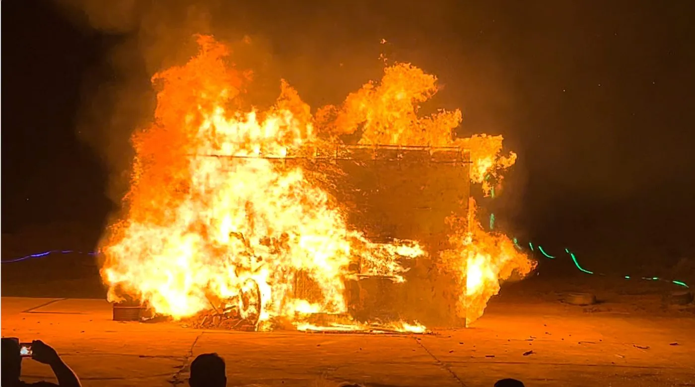 A large fire burning a wooden structure at night.