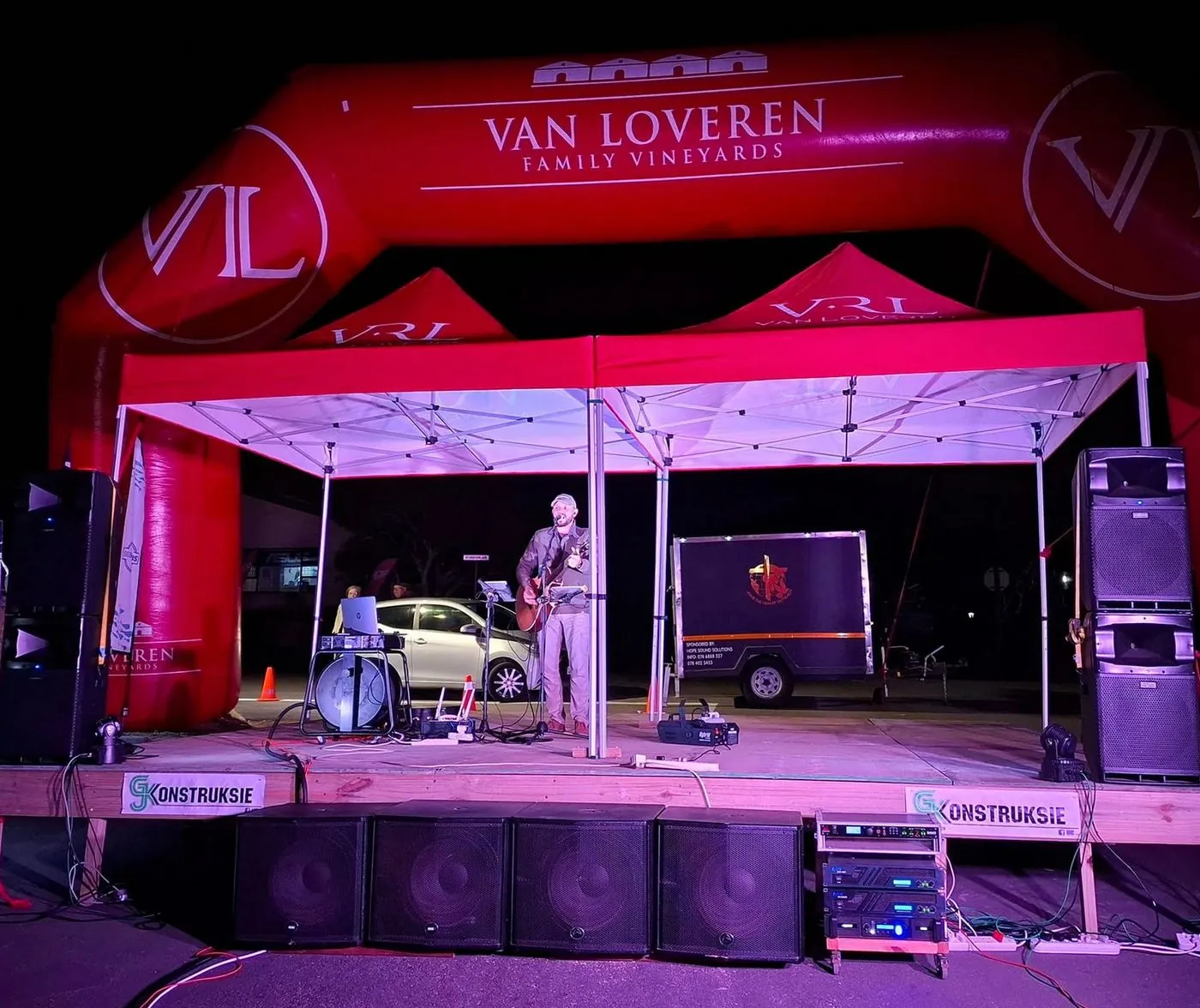 A band performing on a stage under a red inflatable arch branded Van Loveren.