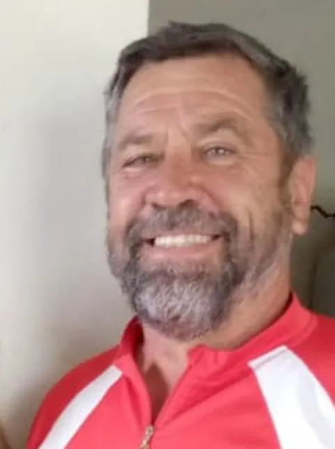 A smiling man with a grey beard in a red and white cycling top.