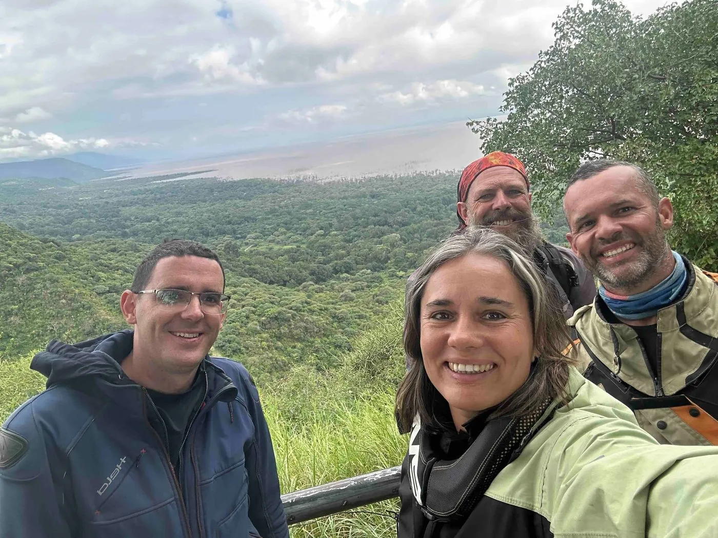 Four people posing for a selfie on a hillside with a wide green valley behind them.