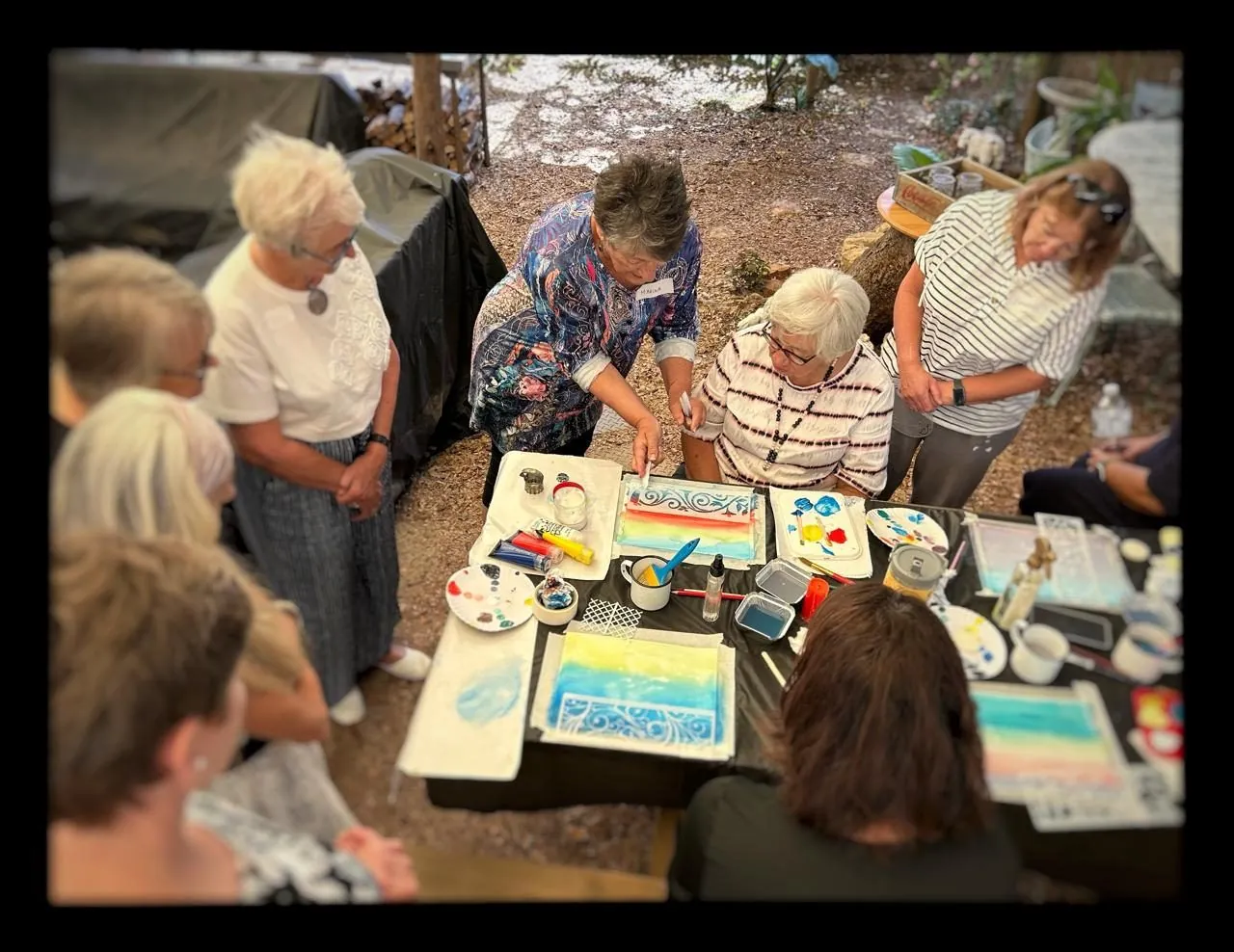 Women seated around tables covered in painted canvases at a workshop.