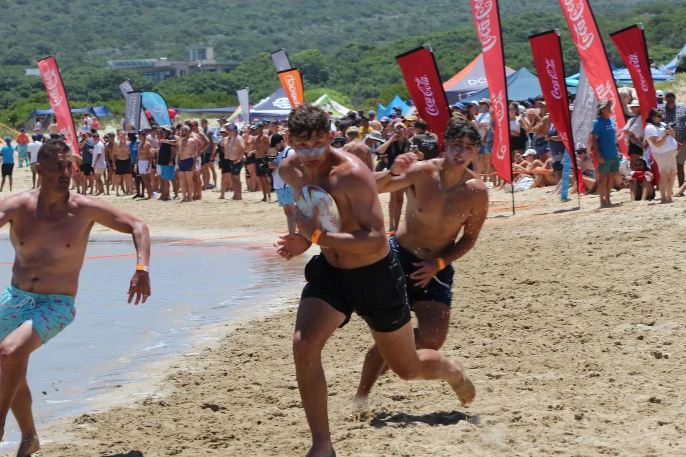 Men running and tackling on a beach during a touch rugby game.