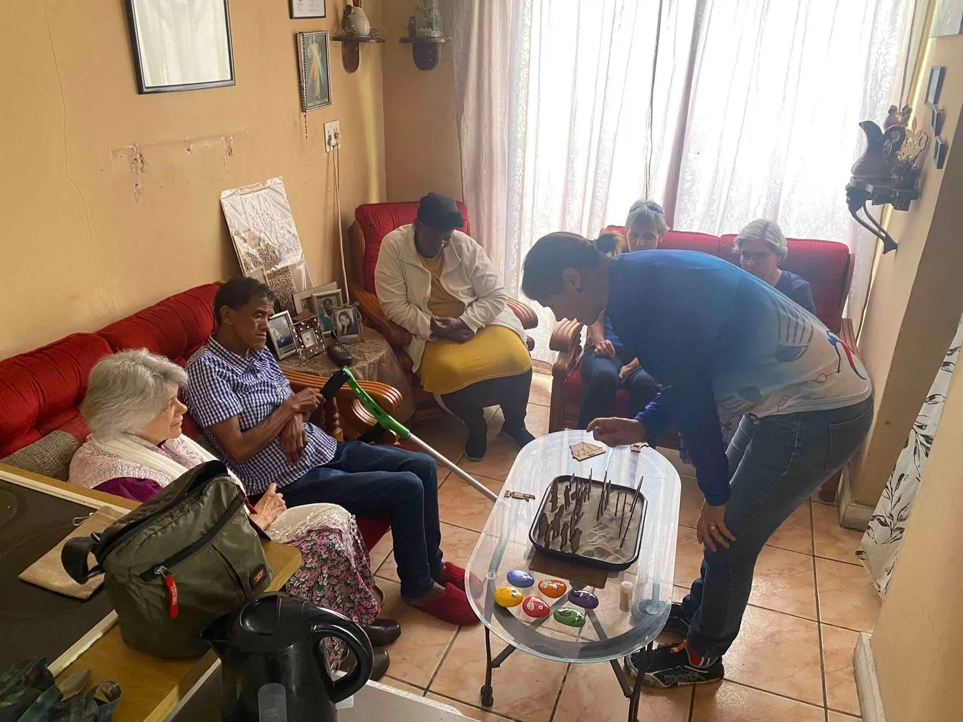 Several people in a small living room; one person bends over a plastic box on the floor while others watch.