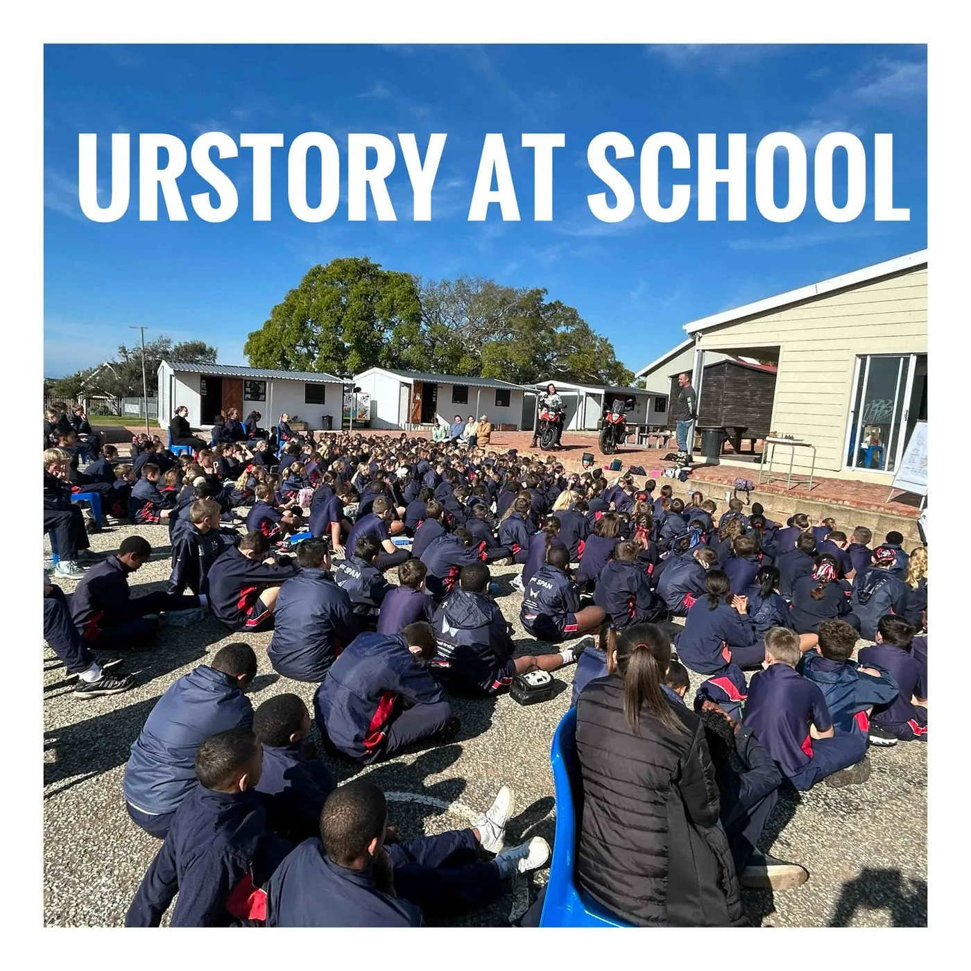 Hundreds of pupils in dark uniforms sitting in rows on a paved school playground, with the heading URstory at school.