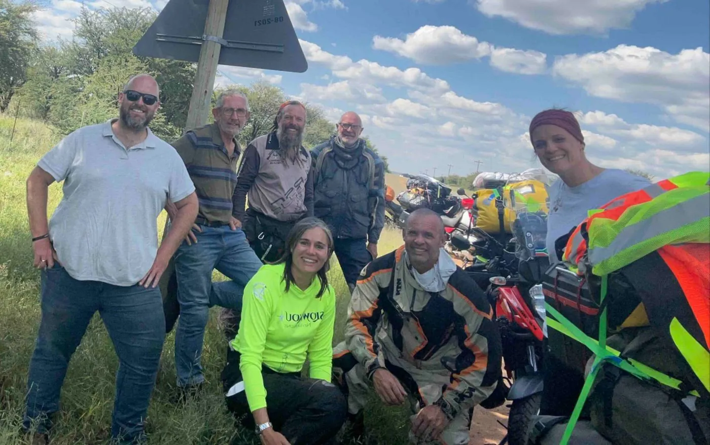 About eight people, some in high-visibility vests, posing in front of parked motorbikes.